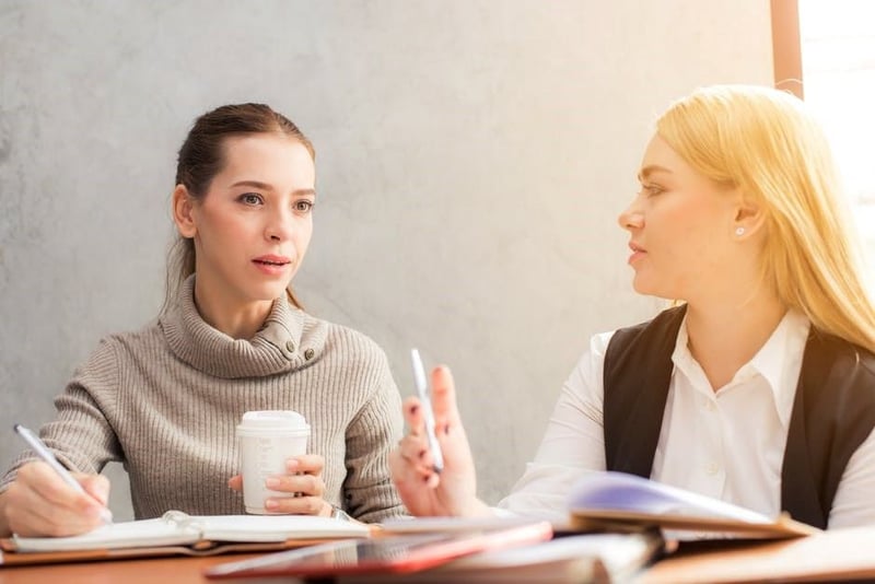 Two colleagues talking across a desk with notebooks, sharing information face to face