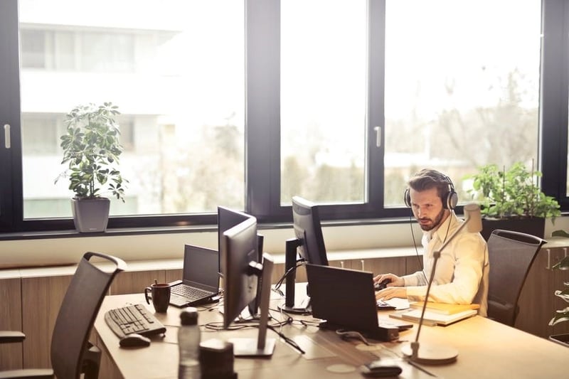 A security professional wearing a headset working at a multi-monitor desk in a bright office