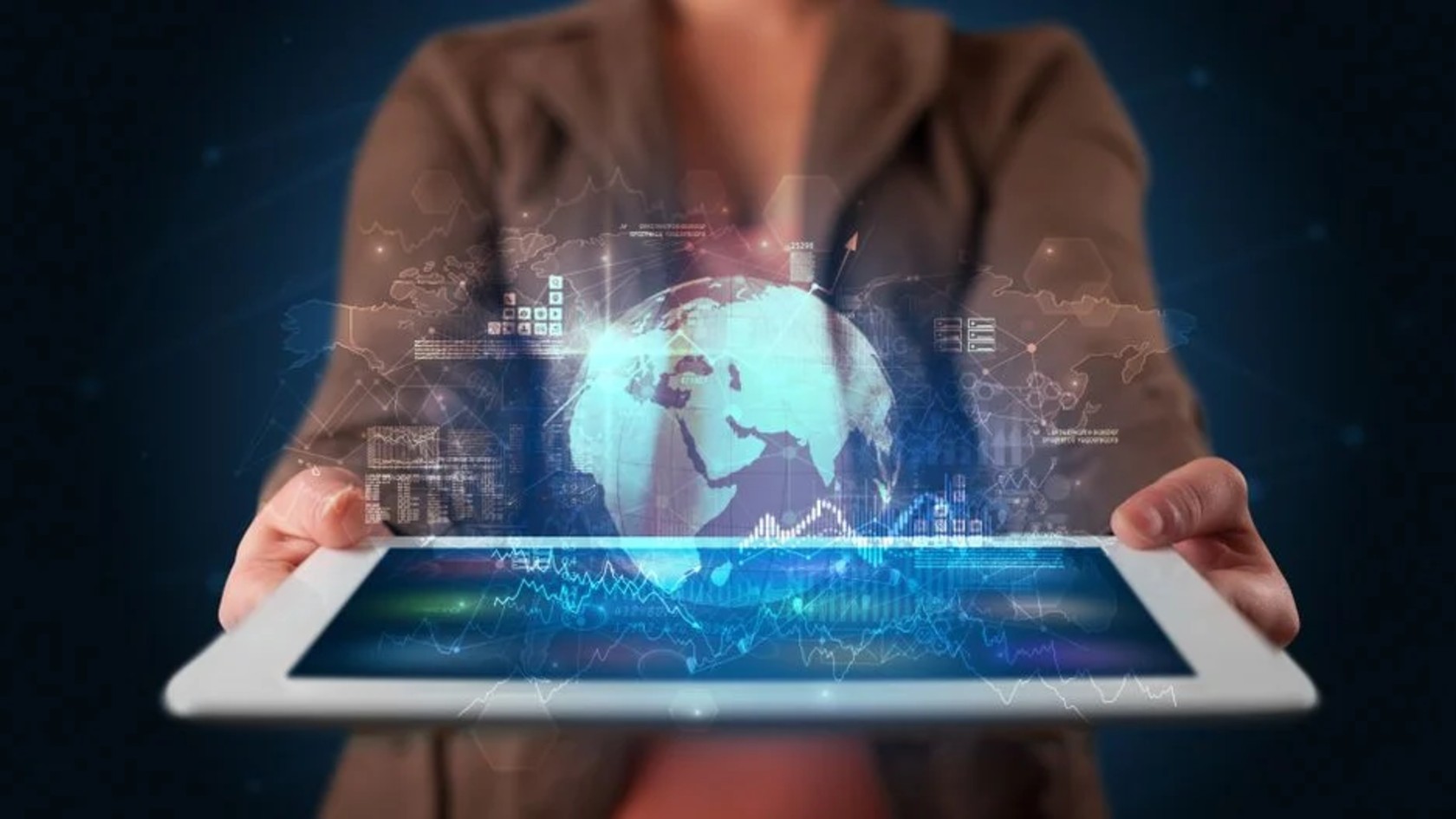 Hand holding a tablet that projects a glowing globe and data charts, representing information security standards for protecting organisational data