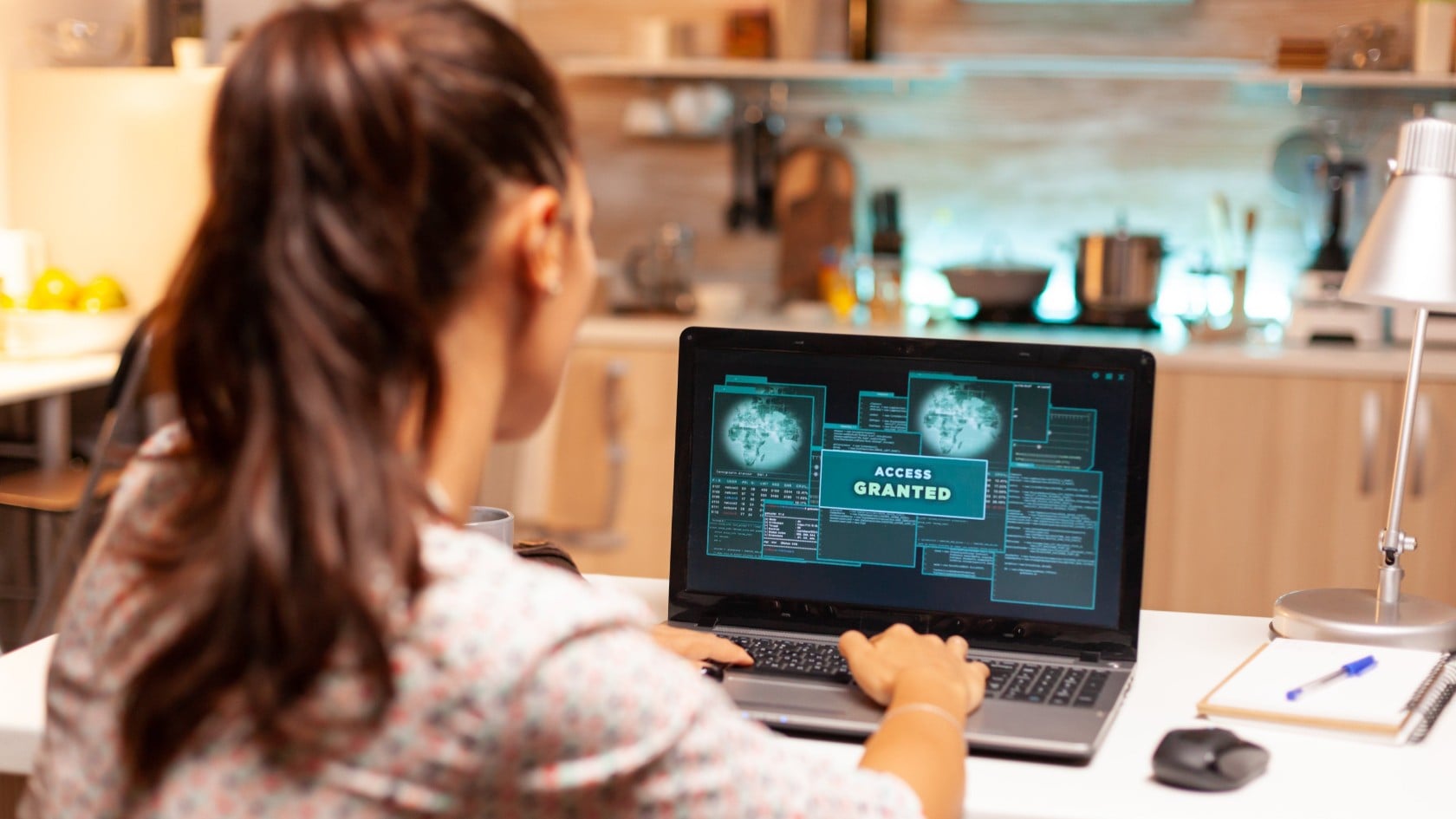 Woman working on a laptop at a kitchen bench, its screen showing an Access Granted security dashboard