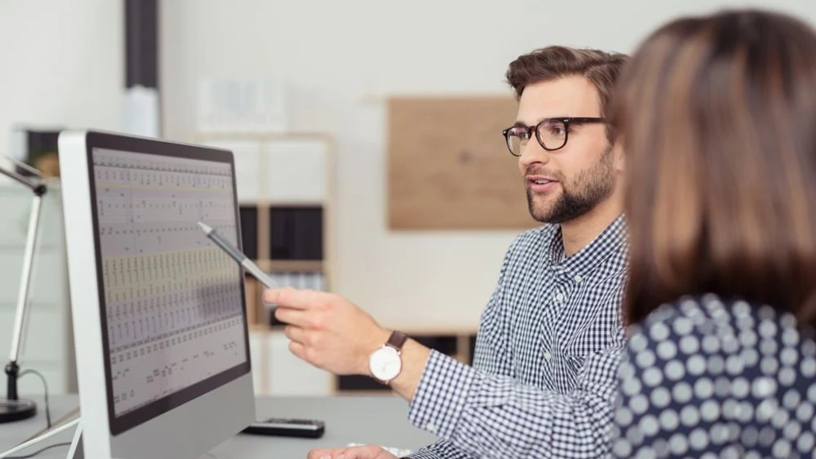 IT professional pointing at data on a desktop monitor while explaining it to a colleague, representing a team reviewing security monitoring results
