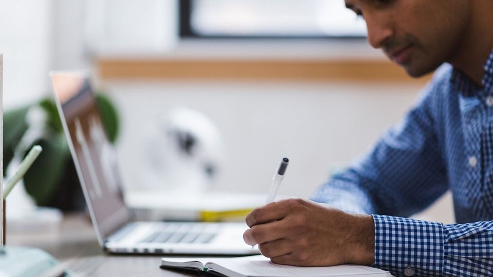 A professional writing notes beside a laptop, representing an organization documenting its incident response plan.