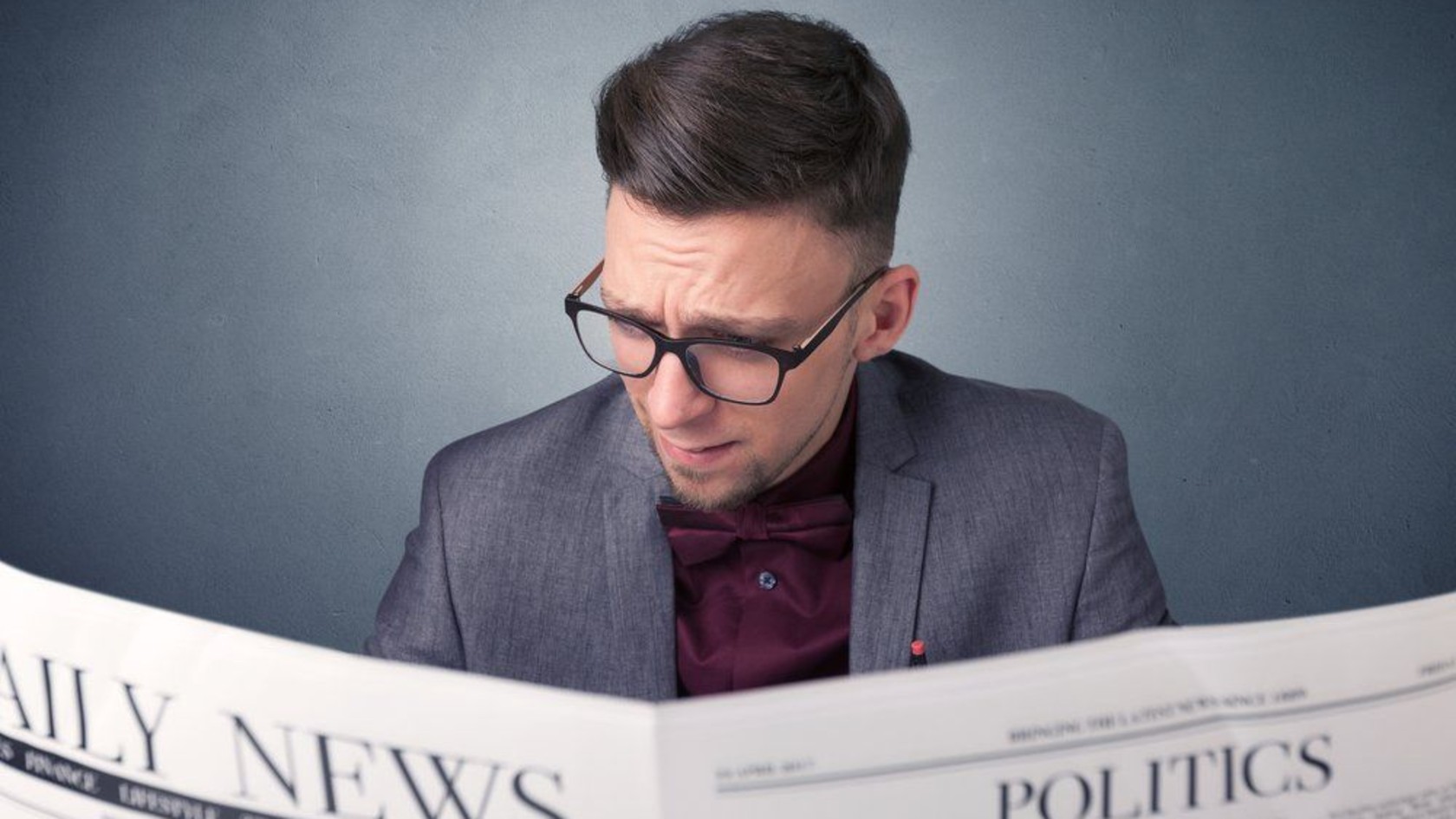Man in glasses and a grey blazer reading a newspaper with a concerned expression, representing keeping up with the ISO 27001:2022 update.