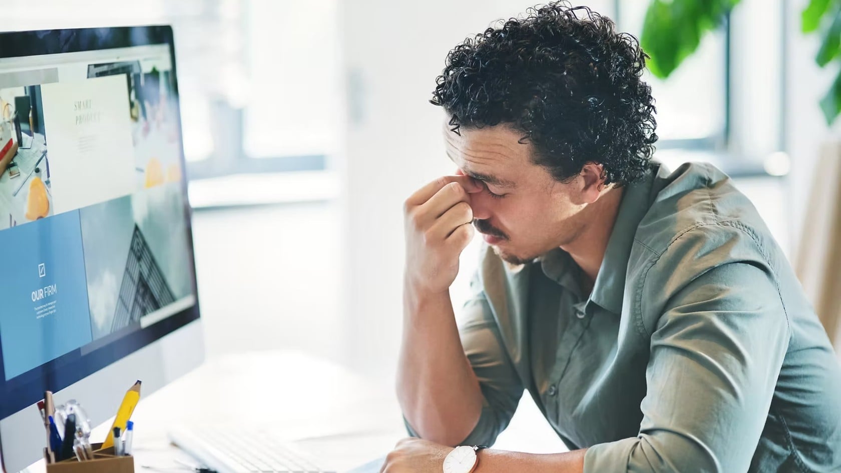 A stressed man pinching the bridge of his nose at his desk in front of a computer, representing the impact of a major data breach.