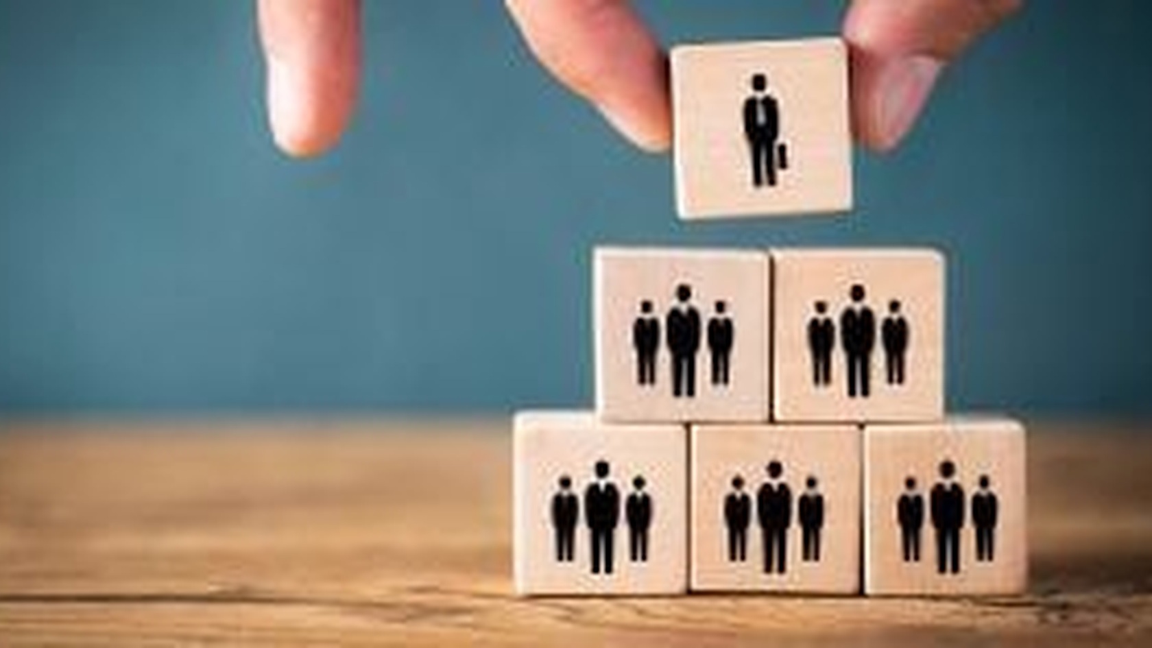 Hand arranging wooden people blocks in a hierarchy, illustrating privileged access roles and permissions.
