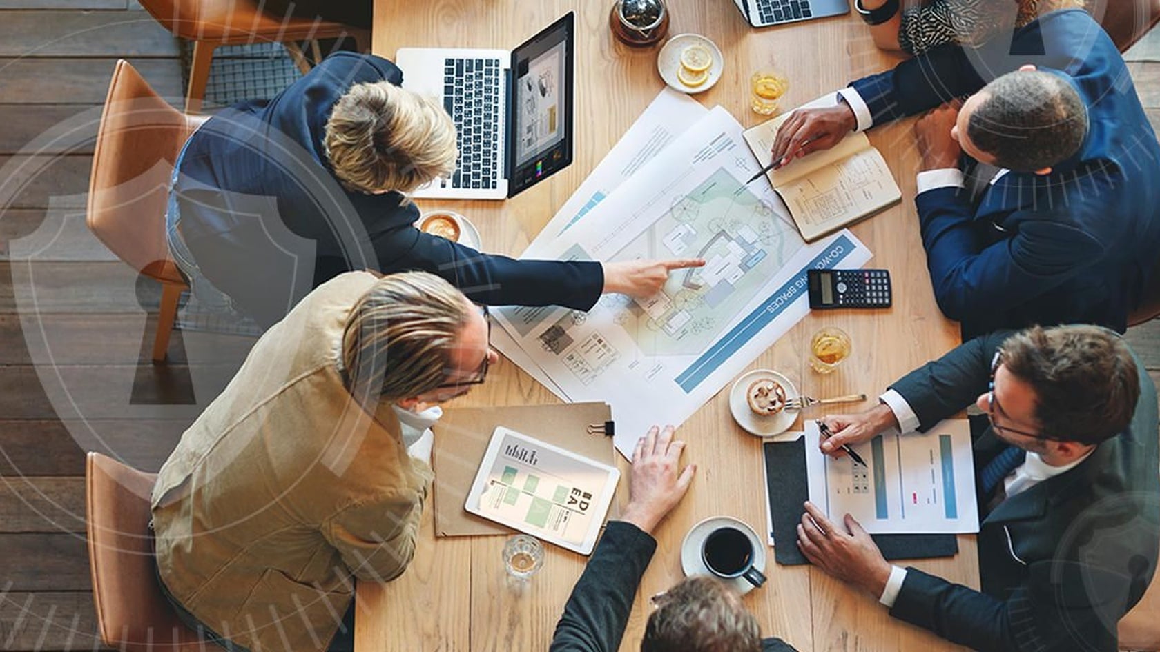 Colleagues collaborating around a meeting table with a security shield overlay, illustrating shared workplace cybersecurity responsibility.