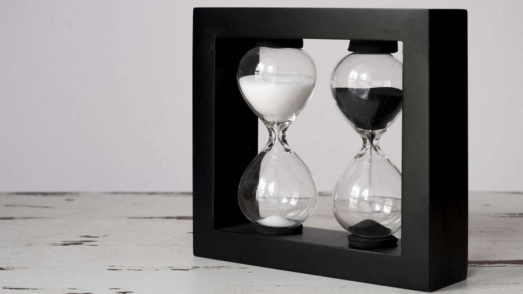 A black double hourglass on a white wooden table, representing the zero days between a software flaw becoming known and attackers exploiting it.